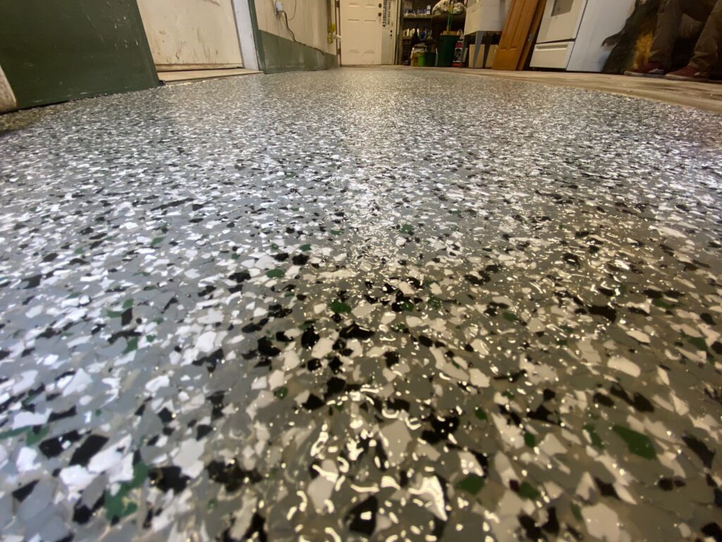 A speckled epoxy floor in a room with white walls and scattered objects, showcasing a reflective, polished surface from a low angle.